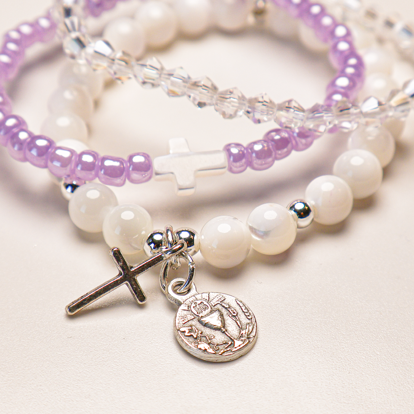 A bracelet set with white and purple beads, silver-tone cross, and a Holy Eucharist medal.