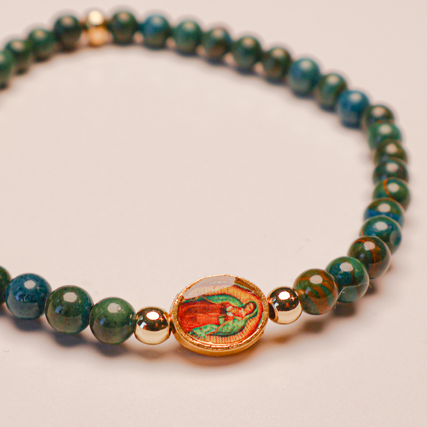 A bracelet with deep green beads and gold-tone accents, featuring an image of Our Lady of Guadalupe in the center.