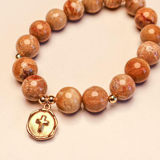 A gold cross bracelet with polished beads, predominantly in earthy tones, featuring a gold-tone cross charm as the central focus.