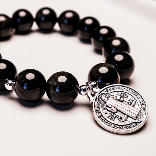 A bracelet with polished black beads and silver-tone accents, featuring a Saint Benedict Medal.